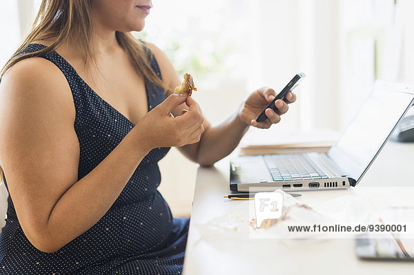 Handy benutzen Frau Büro Kurznachricht essen essend isst Croissant