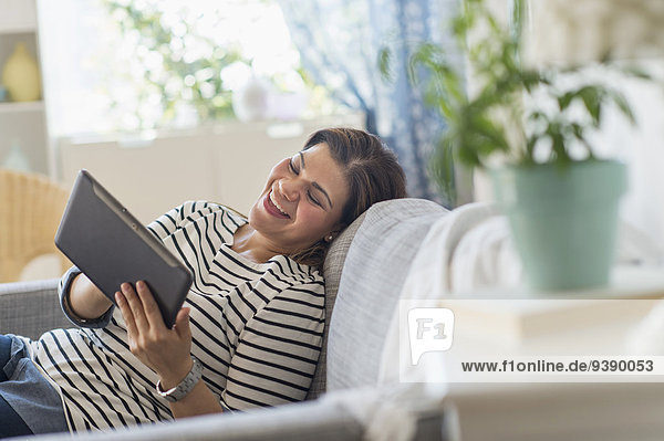 Portrait of happy woman lying on sofa with tablet pc
