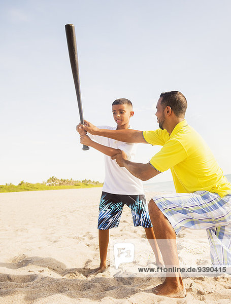 Father and son (10-11) playing baseball on beach