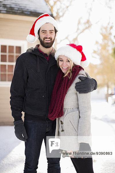 Portrait of young couple in santa hats in front of house