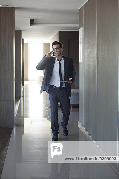 Young businessman talking on phone while walking through office