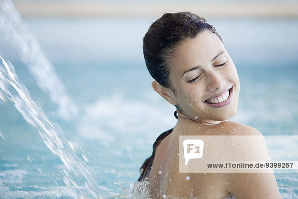 Frau entspannt sich unter dem Springbrunnen im Pool