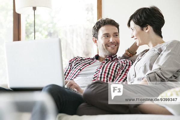 Couple relaxing together on sofa with laptop computer