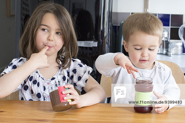 Junge Geschwister schmecken den Inhalt von Gläsern mit den Fingern.