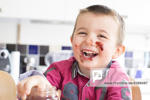 Kleiner Junge mit Marmelade im Gesicht lacht.
