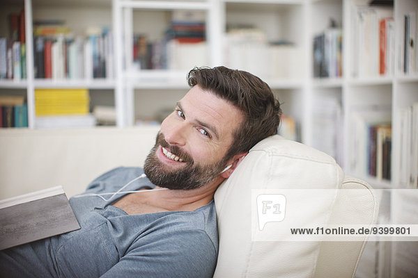 Lächelnder Mann beim Musikhören auf dem Sofa