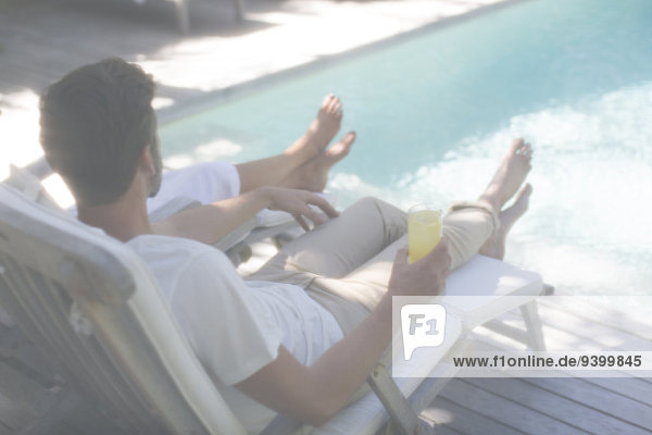 Couple relaxing together in lawn chairs by swimming pool