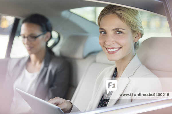 Geschäftsfrau mit digitalem Tablett auf dem Rücksitz im Auto