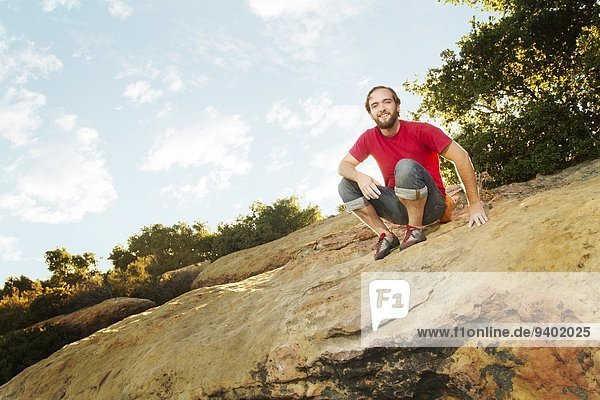 Man sitting on top of sandstone boulder with a grin of success after finishing a bouldering problem.