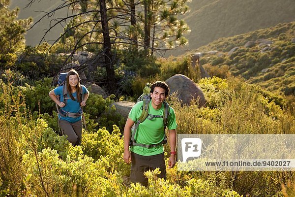 Ethnic couple on a backpacking trip hiking in the mountains through chaparral and pine trees.
