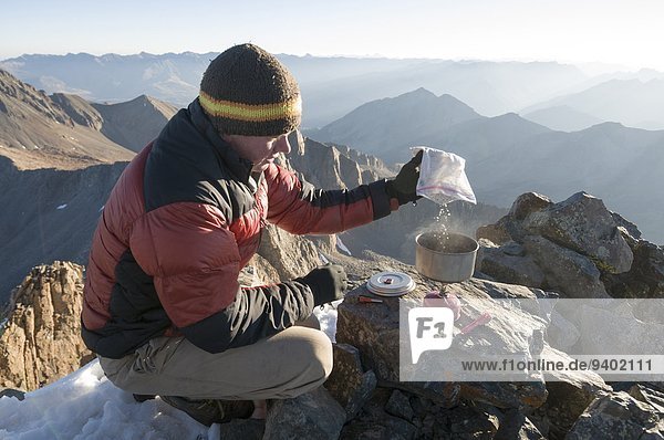 A man boiling water on campstove on the summit of Mount Wilson near Tellride  Colorado.