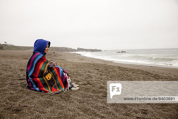 A young woman wrapped in a blanket sits on Wright's Beach  California.