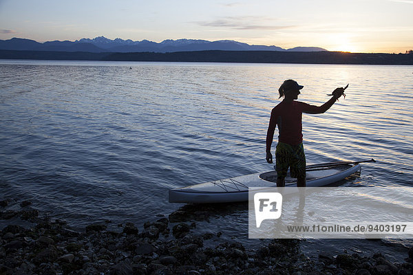 A male stand up paddle boarder (SUP) holds a crab with on the Puget Sound near Poulsbo  Washington.
