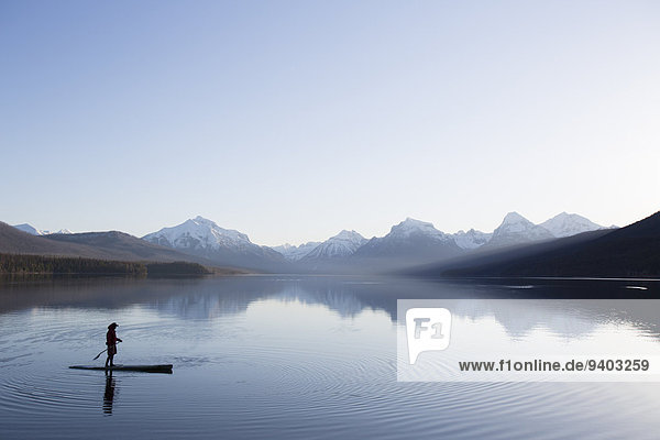 A man stand up paddle boards (SUP) on a calm Lake McDonald in Glacier National Park.