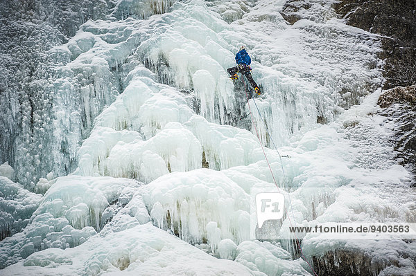 Man lead climbing an ice fall in the middle of a snow storm in Argenti?®re  Chamonix  France.