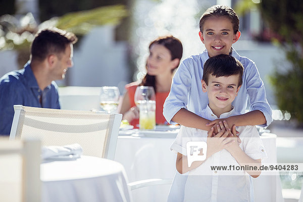 Porträt von lächelnden Geschwistern  Eltern am Tisch sitzend im Hintergrund