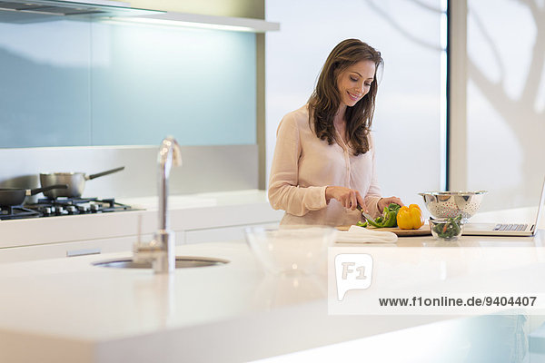 Smiling woman cutting bell peppers at modern kitchen counter