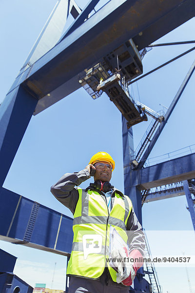 Low angle view of worker talking on walkie-talkie under cargo crane