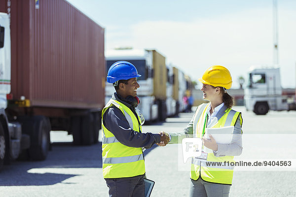 Arbeiter und Geschäftsfrau beim Händeschütteln in der Nähe von Lastwagen und Frachtcontainern