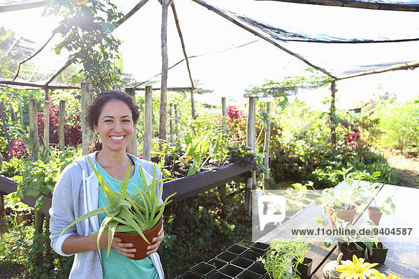 Porträt einer lächelnden Frau mit Topfpflanze im Gewächshaus