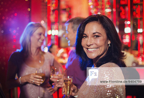 Portrait of smiling woman holding champagne flute in night club  people in background