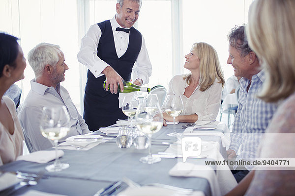 People sitting at restaurant table  waiter pouring white wine