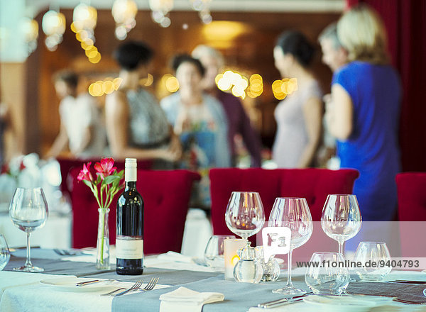 Weingläser und Flasche Rotwein auf dem Tisch im Restaurant,  Menschen im Hintergrund