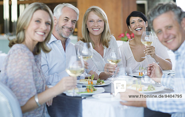 Porträt von lächelnden Menschen beim Toasten mit Weißwein im Restaurant
