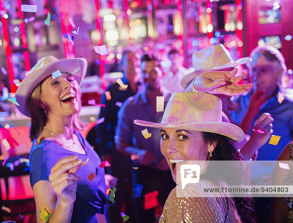 Konfetti fallen auf Frauen mit Cowboyhüten  lachend und tanzend im Nachtclub.