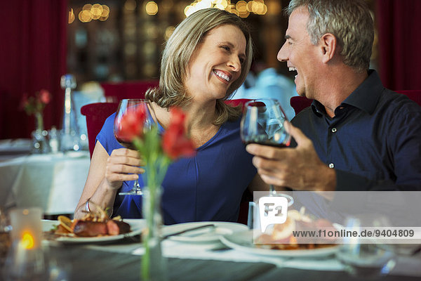 Lächelndes  reifes Paar  das sich ansieht und Gläser mit Rotwein im Restaurant hält.