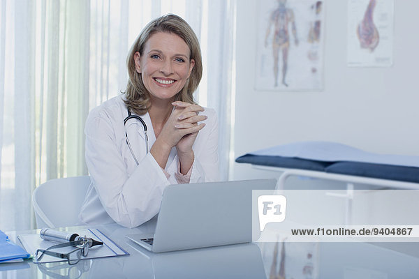 Portrait of smiling female doctor sitting at desk with laptop