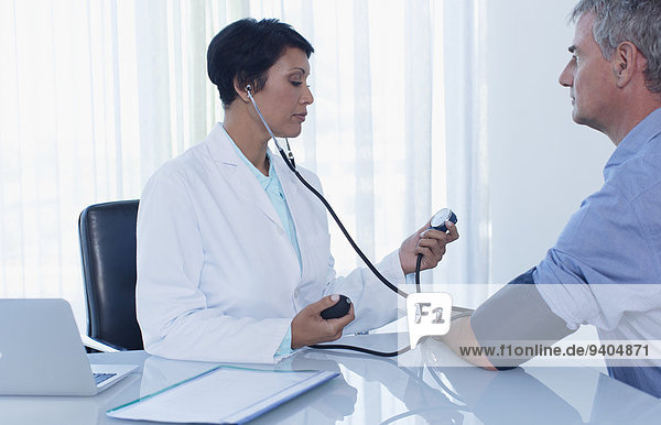 Female doctor taking patient's blood pressure in office