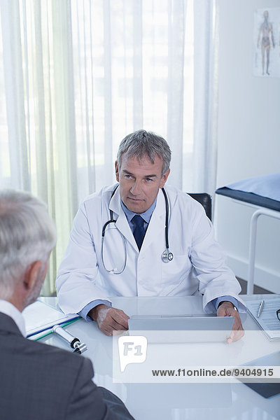 Mature doctor with laptop and man sitting at desk in office