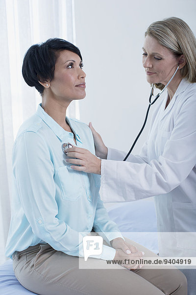 Female doctor examining her patient with stethoscope in office