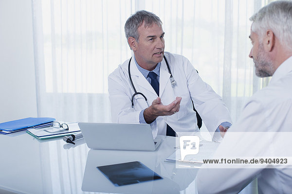 Mature doctor talking to patient at desk in office