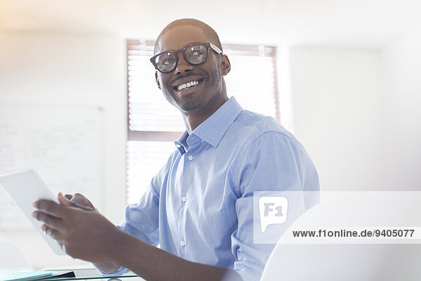 Porträt eines jungen Geschäftsmannes mit Brille und blauem Hemd mit digitalem Tablett im Büro
