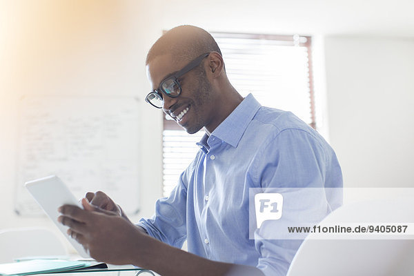 Lächelnder junger Geschäftsmann mit Brille und blauem Hemd mit digitalem Tablett im Büro