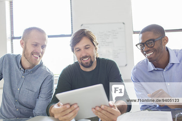Drei lächelnde Männer bei der Arbeit mit dem digitalen Tablett im Büro
