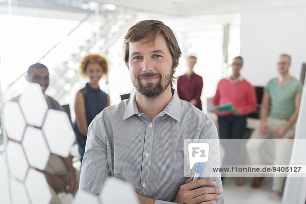 Porträt eines lächelnden Geschäftsmannes im grauen Hemd  Büroteam im Hintergrund