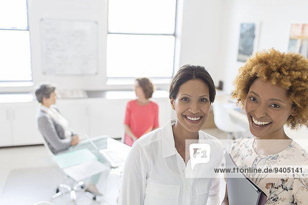 Porträt von zwei lächelnden Geschäftsfrauen im Büro  Kollegen im Hintergrund