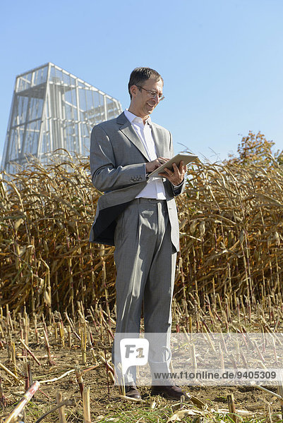 Businessman with digital tablet in cornfield  geothermal power station in background