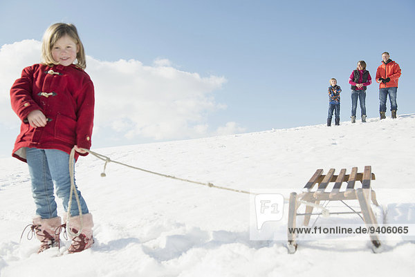 Girl with sledge  family standing in background