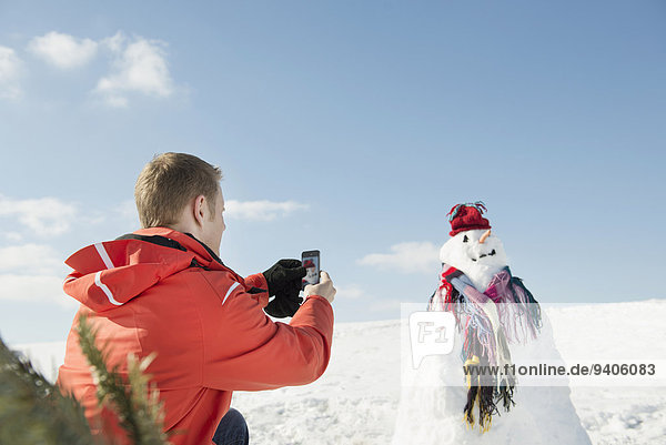 Man taking picture of snowman with smart phone