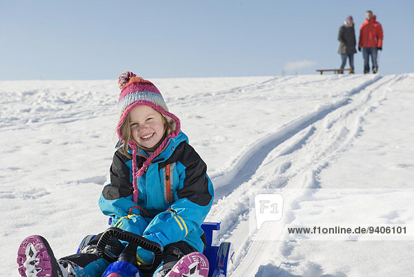 Portrait of girl sledging down hill while her parents watching