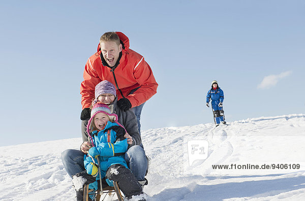 Father  mother and daughter sledging down hill while son watching them
