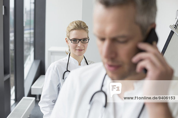Doctor on phone while female doctor in background