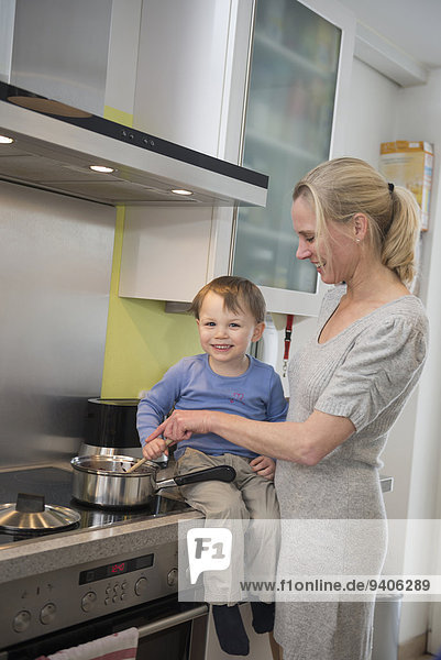 Boy helping his mother stirring food in pot  smiling
