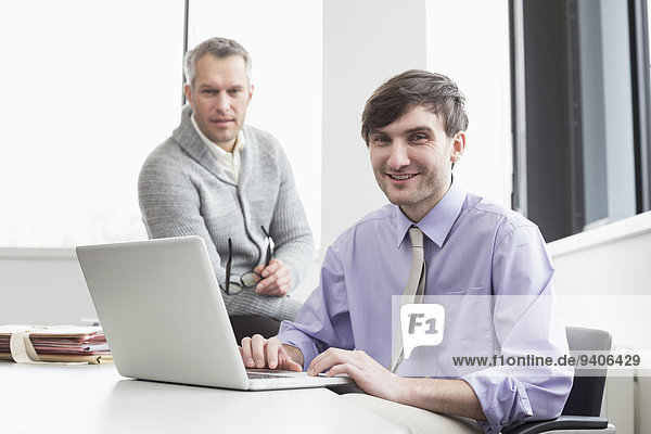 Businessmen using laptop in office  smiling