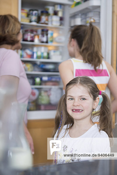 Portrait of girl  grandmother and sister looking into refrigerator in background