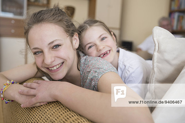 Portrait of sisters sitting on couch in living room  smiling